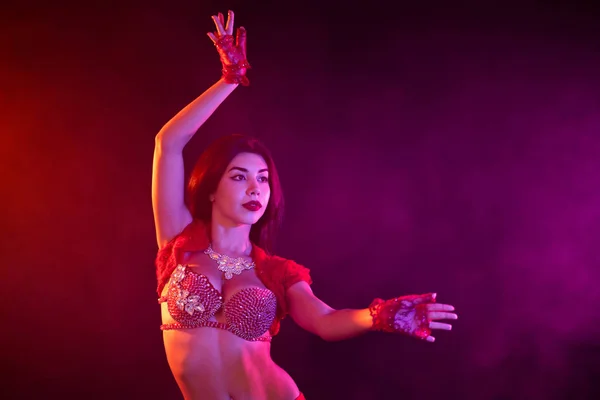 Frestande sexig traditionella orientaliska magdansös flicka dansa på lila neon rök bakgrund. Kvinna i exotiska röd kostym flyttar sexuellt sin halvnakna kropp. — Stockfoto