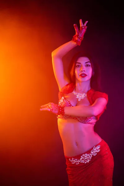 Спокуслива сексуальна традиційна дівчина танцює на фіолетовому неоновому тлі диму. Жінка в екзотичному червоному костюмі сексуально рухає її напівголим тілом . — стокове фото
