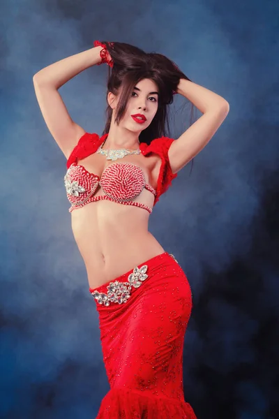 Woman in exotic shining red costume sexually moves her body. Sexy traditional oriental belly dancer girl dancing on neon smoke background. Muslims, temptation concept — Stock Photo, Image