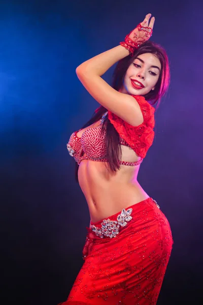 Frestande sexig traditionella orientaliska magdansös flicka dansa på lila neon rök bakgrund. Kvinna i exotiska röd kostym flyttar sexuellt sin halvnakna kropp. — Stockfoto