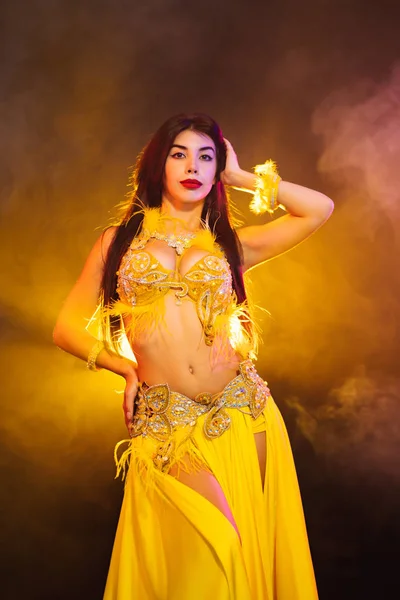 Alluring sexy traditional oriental belly dancer girl dancing on yellow neon smoke background. Woman in exotic costume with feathers sexually moves her semi-nude body — Stock Photo, Image
