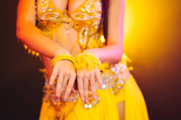 Close up of traditional oriental belly dancer girls hands posing on yellow neon smoke background. Unrecognizable woman in exotic costume with feathers — Stock Photo, Image