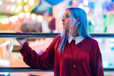 Hippi kız mavi boyalı saç ve payetler çiller olarak. Kırmızı giyim ve burun piercing, şeffaf gözlük, kulakları kadında tüneller, eğlence parkı içinde sıradışı saç modeli