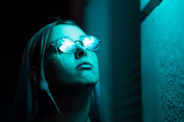 Bin yıllık gizemli güzel kızla gece parlak neon duvarının yakınında alışılmadık boyalı saç modeli. Saç, altın pullu çiller olarak mavi, piercing burun. Gizemli hipster genç gözlük