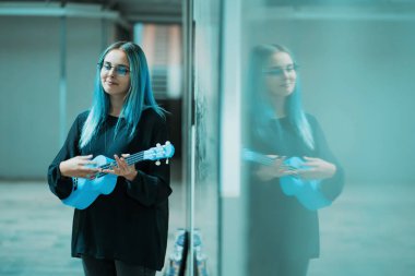 Genç güzel kız mavi saçlı mavi ukulele Altgeçit veya Metro oynamak.