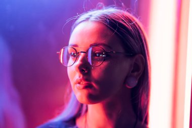 Bin yıllık gizemli güzel kızla gece parlak neon duvarının yakınında alışılmadık boyalı saç modeli. Saç, altın pullu çiller olarak mavi, piercing burun. Gizemli hipster genç gözlük
