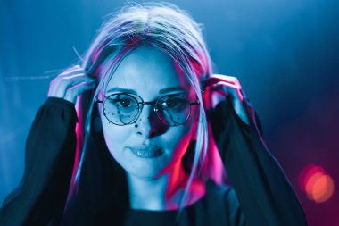Bin yıllık gizemli güzel kızla gece parlak neon duvarının yakınında alışılmadık boyalı saç modeli. Saç, altın pullu çiller olarak mavi, piercing burun. Gizemli hipster genç gözlük