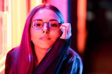 Bin yıllık gizemli güzel kızla gece parlak neon duvarının yakınında alışılmadık boyalı saç modeli. Saç, altın pullu çiller olarak mavi, piercing burun. Gizemli hipster genç gözlük