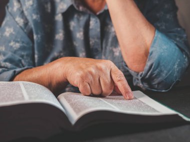 Yaşlı kadın evde kalın bir kitap okuma. İncil ile büyükanne. Konsantre yaşlı emekli kırışıklıkları elleri ile kağıt sayfa kitaplığı'nda parmak dikkatle takip