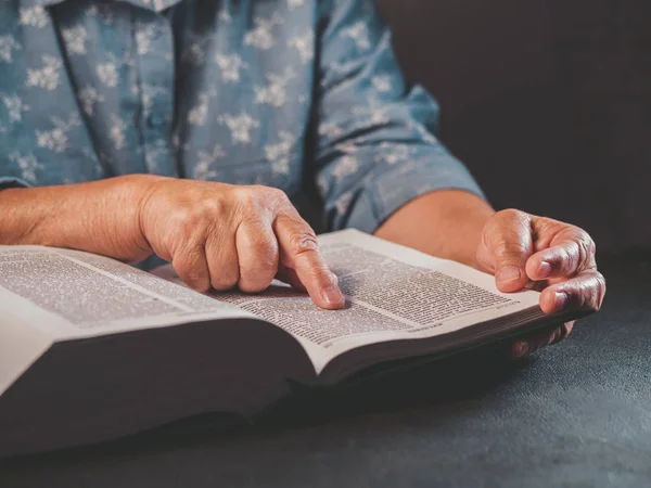 Vieille femme lisant un livre épais à la maison. Grand-mère avec la Bible. Pensionné âgé concentré avec des rides sur les mains suit attentivement doigt sur papier page dans la bibliothèque — Photo