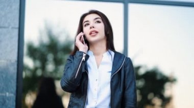 İş kadını ile smartphone ofis binası yakınında kapatın. Kız cep telefonu ile konuşma var. Güzel beyaz genç kadın ile hareket eden aygıt söz.