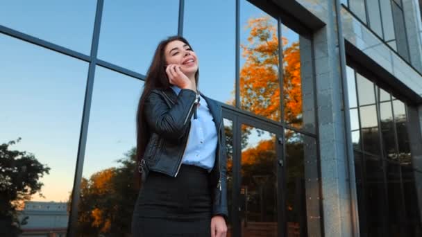 İş kadını ile smartphone ofis binası yakınında kapatın. Kız cep telefonu ile konuşma var. Güzel beyaz genç kadın ile hareket eden aygıt söz. — Stok video