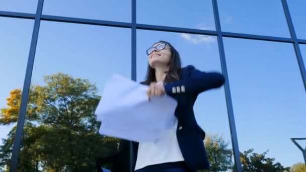 Joven empresaria celebra el éxito y tirar papeles y documentos al aire en el fondo moderno edificio de oficinas. Libertad, finalización exitosa del concepto de proyecto — Vídeo de stock