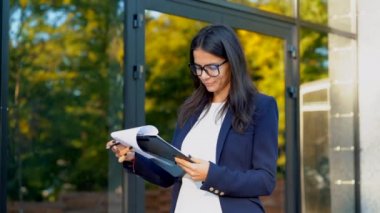 Genç güzel esmer kadın takım elbise ve gözlük belgeleri, faturalar, rapor denetler. Ofis Binası yakınında duran işkadını. Personel iş ile memnun olduğunu