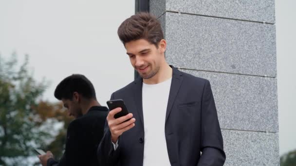 Biznesmen przy użyciu telefonu komórkowego dla wiadomości tekstowych. Za pomocą aplikacji business na smartfona w tle budynek biurowy przystojny mężczyzna. 4k — Wideo stockowe