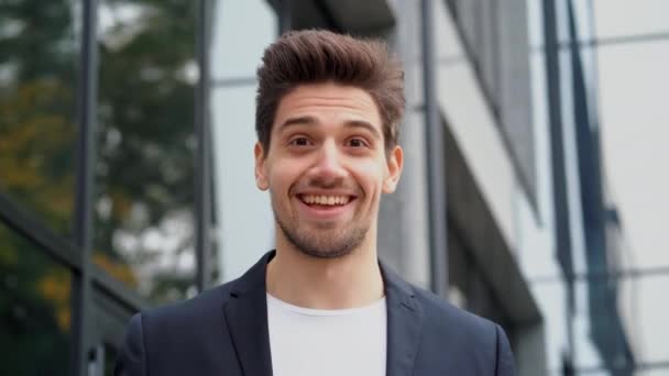 Smiling happy student man showing eureka gesture. Portrait of young thinking pondering businessman having idea moment pointing finger up on office building background — Stock Video