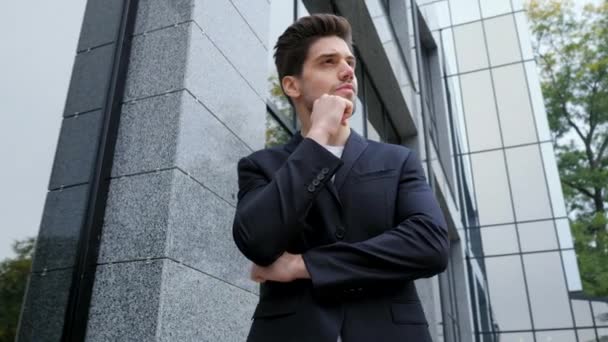 Retrato do empresário pensativo bem sucedido na cidade. Homem de casaco de fato de negócios no fundo do edifício de escritórios. Uma pessoa bonita pondera sobre o trabalho. Câmera se move da direita para a esquerda — Vídeo de Stock