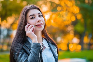 İş kadını smartphone ile yakından sonbahar günbatımı ışık parkında. Kız cep telefonu ile konuşma var. Güzel beyaz genç kadın ile hareket eden aygıt söz