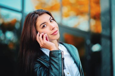 İş kadını ile smartphone ofis binası yakınında kapatın. Kız cep telefonu ile konuşma var. Güzel beyaz genç kadın ile hareket eden aygıt söz.