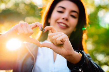 Sevgi jesti gösterilen ve kameraya gülümseyen genç güzel kadın.
