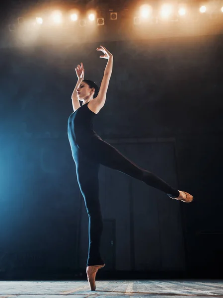Jonge mooie ballerina rook werkgebied modern ballet dansen. Hiermee voert u vloeiende bewegingen met handen tegen de achtergrond van de schijnwerpers. Vrouw in zwarte kostuum op scène — Stockfoto