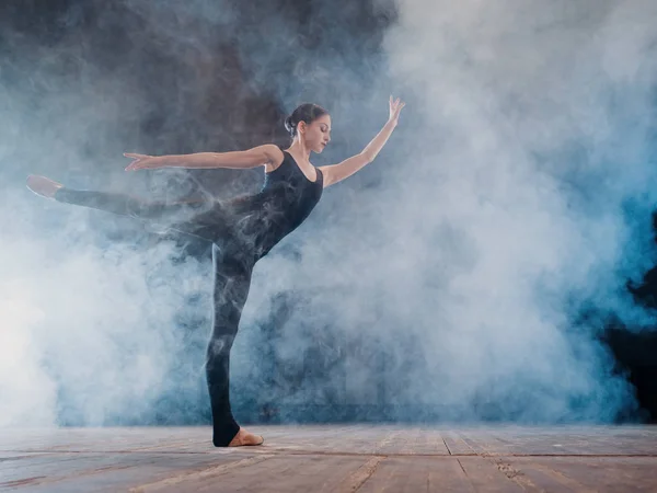 Giovane bella ballerina sul palcoscenico di fumo danza balletto moderno. esegue movimenti fluidi con le mani sullo sfondo dei faretti. Donna in costume nero sulla scena — Foto Stock