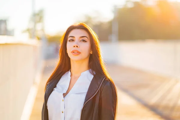 Portrait of young happy business woman in the city. Beautiful caucasian student girl in white sexy blouse standing in the autumn street in sunset light.