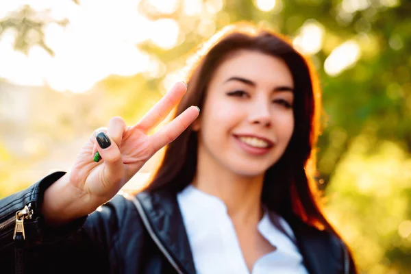 Молодая красивая женщина показывает жест МИРА и улыбается в камеру на фоне осеннего парка . — стоковое фото