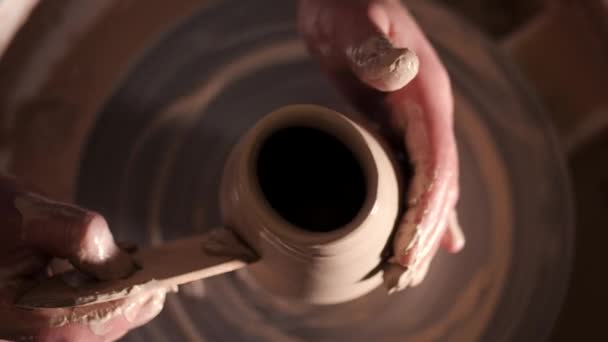 Upplevt potter former lera produkten - kannan - med keramik verktyg. Närbild av manliga händer arbetar på keramiker hjul. Skott av halva-färdig keramik vas spinning på jigger. — Stockvideo
