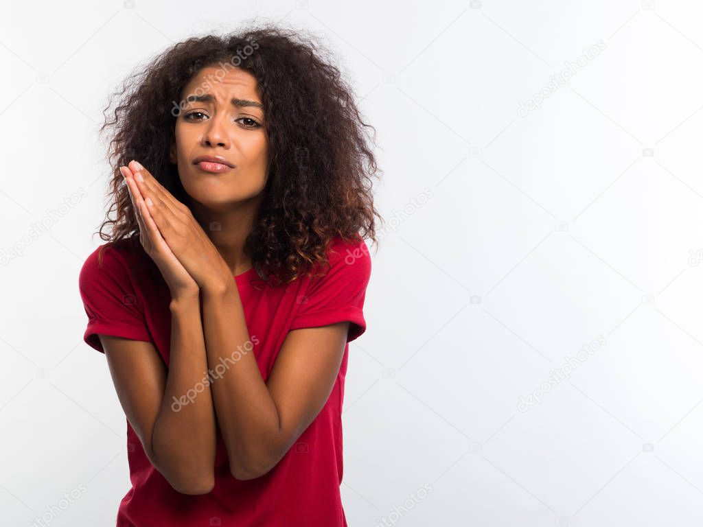Attractive african woman in red t-shirt praying, begs over white background. Mixed race girl begging someone