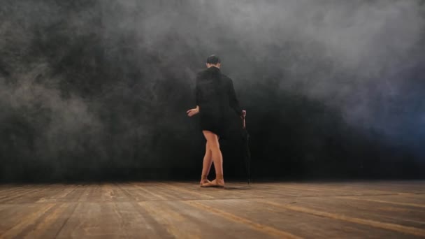 Bailarina en chaqueta larga negra en body sexy bailando en el escenario con luz mágica y humo, cámara lenta. Joven bailarina atractiva en zapatillas de ballet puntas con paraguas — Vídeos de Stock