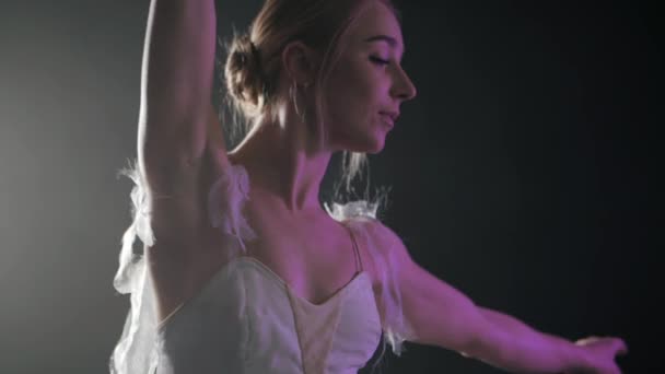 Bailarina sensual graciosa no vestido de tutu branco elementos de dança do balé clássico ou moderno no escuro com luz roxa e fumaça no fundo preto, câmera lenta — Vídeo de Stock