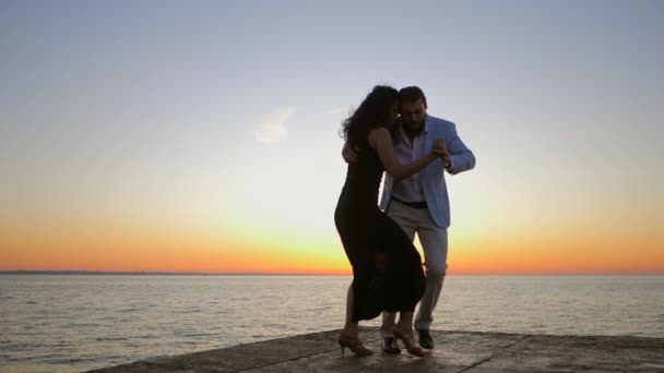 Portrait de jeune couple attrayant dansant bachata latine près de la mer ou de l'océan. Fond de lumière du soleil. Heure d'été, images romantiques. Mouvement lent — Video