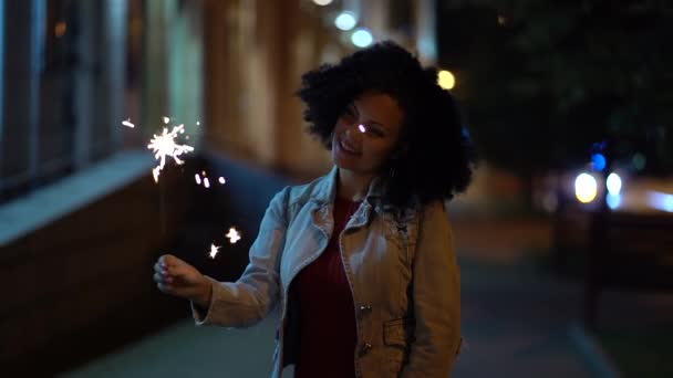 Mladá krásná žena s velmi kudrnaté afro vlasy tančí s ohněm Bengálsko v noci osvětlené ulice. Neobvyklé módní dívka s prskavky. Dovolená concept. Slow motion záběry. — Stock video