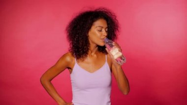 Şişe pembe duvar arka plan üzerinde su içme çekici Afro-Amerikan sportif genç kadın. Spor giysileri fitness sonra kızı. Stüdyo görüntüleri. 4k