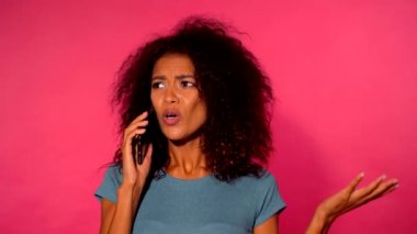 Kızgın Afrikalı-Amerikalı kadın ile smartphone pembe duvar arka plan üzerinde yeşil t-shirt yapma çağrısında kıvırcık saçlı. Kız gergin, huzursuzluk ve kızgınlık ifade eder.