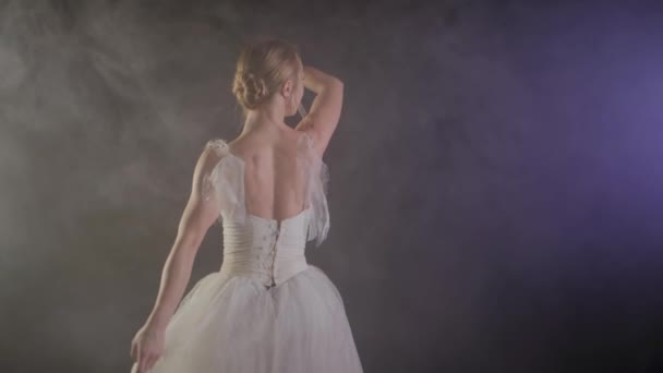 Elegante bailarina en vestido blanco bailando elementos de ballet clásico o moderno en la oscuridad con luz y humo sobre el fondo negro, cámara lenta — Vídeos de Stock