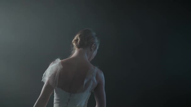 Graceful ballerina in white dress dancing elements of classical or modern ballet in the dark with light and smoke on the black background, slow motion — Stock Video