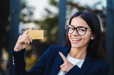 Kamera ve gösteren sınırsız gold kart ofis binası arka plan üzerinde başarılı güzel kadın göz. Gözlük ve takım elbise giyen profesyonel kadın Yöneticisi