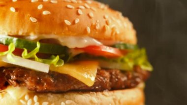 Sulu biftek burger göğsü, soğan, sebze, eritilmiş peynir, marul, sos ve susam tepesinde. İzole hamburger koyu duman arka plan üzerinde yakından görmek döner.