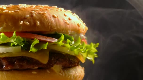 Obří lahodné čerstvé burger otočení na tmavé kouřové pozadí. Cheeseburger zobrazení makra. Americká fastfood, nezdravého tuku mňam jídlo koncept.