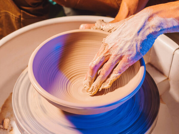 Creating earthenware and traditional pottery concept. Experienced male potters hands creating beautiful clay product - bowl - using professional tools. Toned cinematic, craft factory authentic