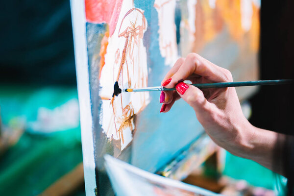 Woman paints a painting on canvas. Art academy or drawing school. Girl paints on the easel. Only hand of unknown artist, brush and canvas.