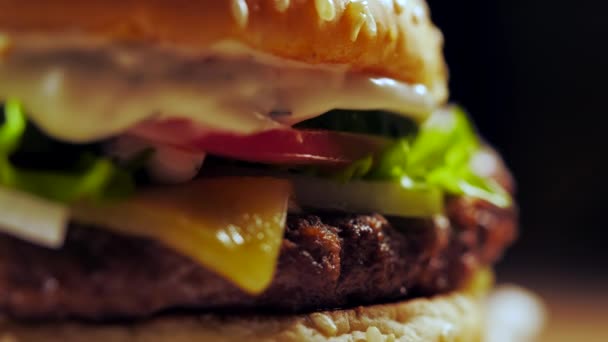 Gran hamburguesa apetitosa con chuleta de carne, cebolla, verduras, queso derretido, lechuga y salsa de mayonesa. Hamburguesa aislada gira sobre fondo de humo oscuro, vista de cerca — Vídeos de Stock