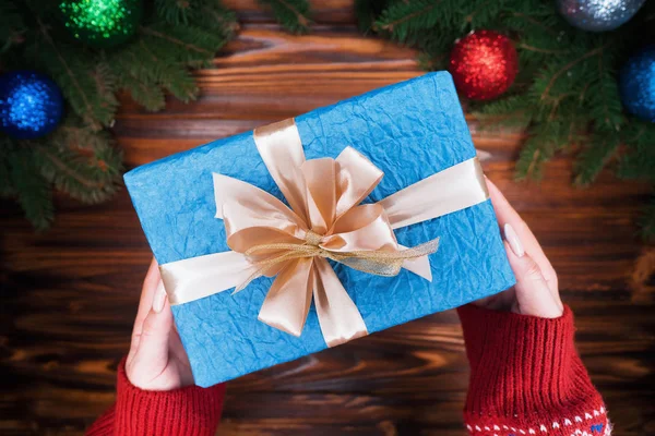 顶部视图 女人的手与礼物包裹在蓝色的纸与金色的丝带 木制复古桌 美丽的假日背景与绿色云杉分支装饰圣诞球 — 图库照片
