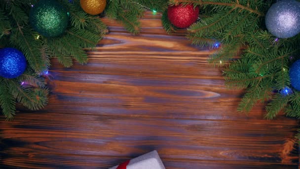 Wooden table with Christmas decorations. Cat paws giving gift wrapped in silver shining paper and red bow. Top plan view. Animal, pets, new year concept. Slow motion. — Stock Video