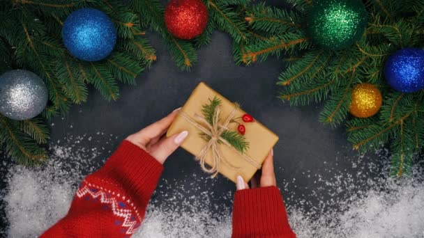 Kadının el çam dalları ve kar ile yapılan çerçeve merkezinde Kraft kağıt sarılı hediye koyar ve sonra alır. Noel süsleri - baubles Garland ışıklar yanıp sönüyor — Stok video