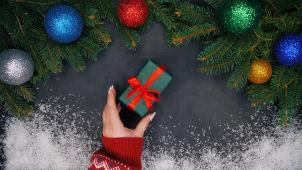 梨花の手モミの枝と雪で作られたフレームの中央に緑色の紙で包まれた贈り物を置くし それを取る クリスマスの装飾 つまらないものガーランド ライトが点滅 — ストック動画