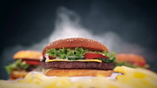 Friss fincsi hamburgerek roston sült forog a fekete füst háttér. Hús patty, paradicsom, uborka, fejes saláta és a sesame magok. Fast food koncepció. gyorsétel életmód — Stock videók