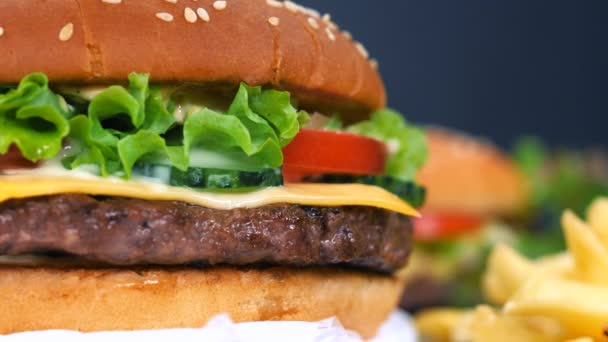 Velké chutné burger s řízek masa, zeleninu, sýr, ledový salát a omáčka. Hamburger se otočí na jiné jídlo pozadí, detailní zobrazení. Koncept nezdravých dobrot.